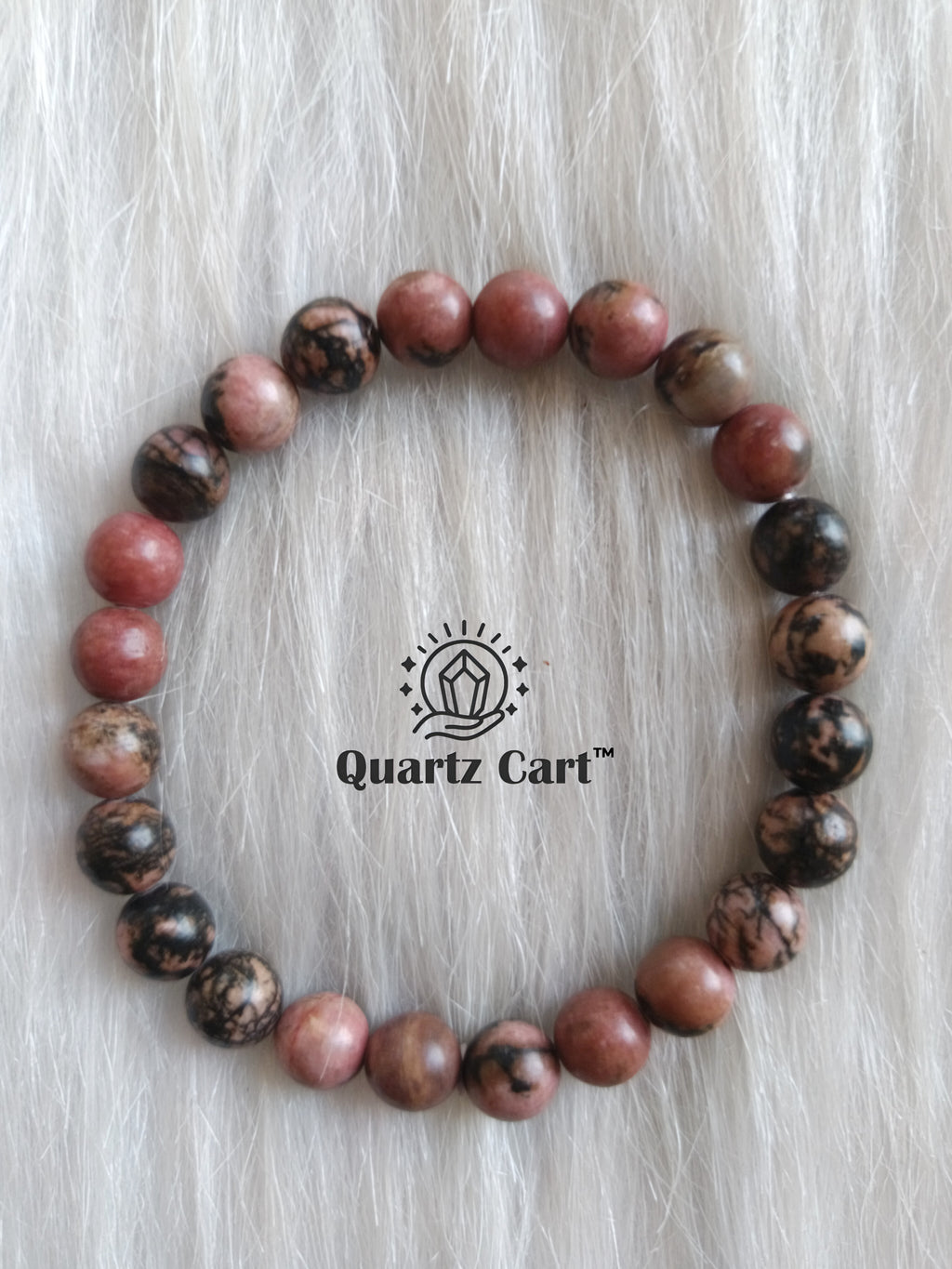 Rhodonite crystal bracelet with polished beads placed on surface for heart chakra healing and inner balance