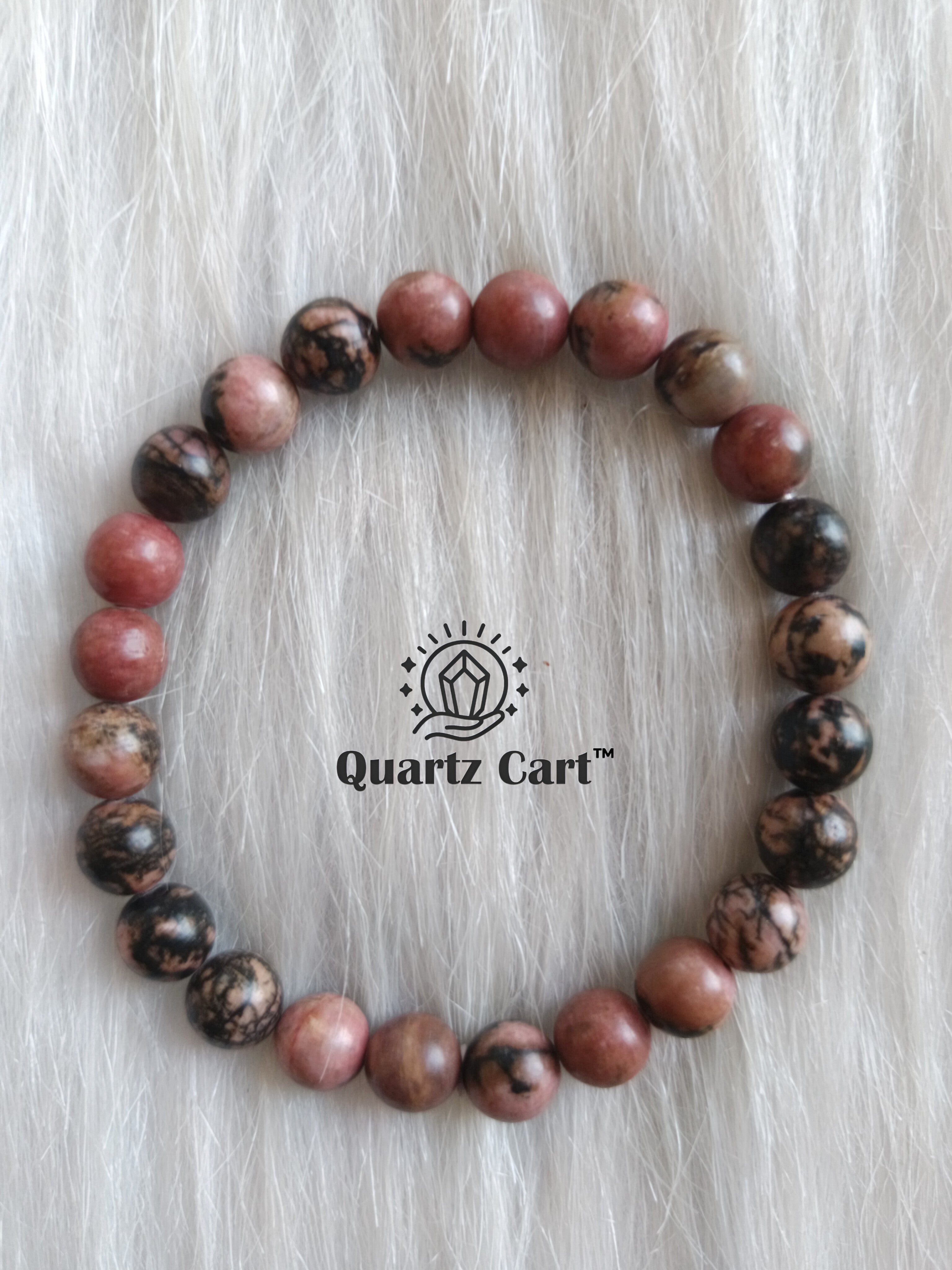 Rhodonite crystal bracelet with polished beads placed on surface for heart chakra healing and inner balance