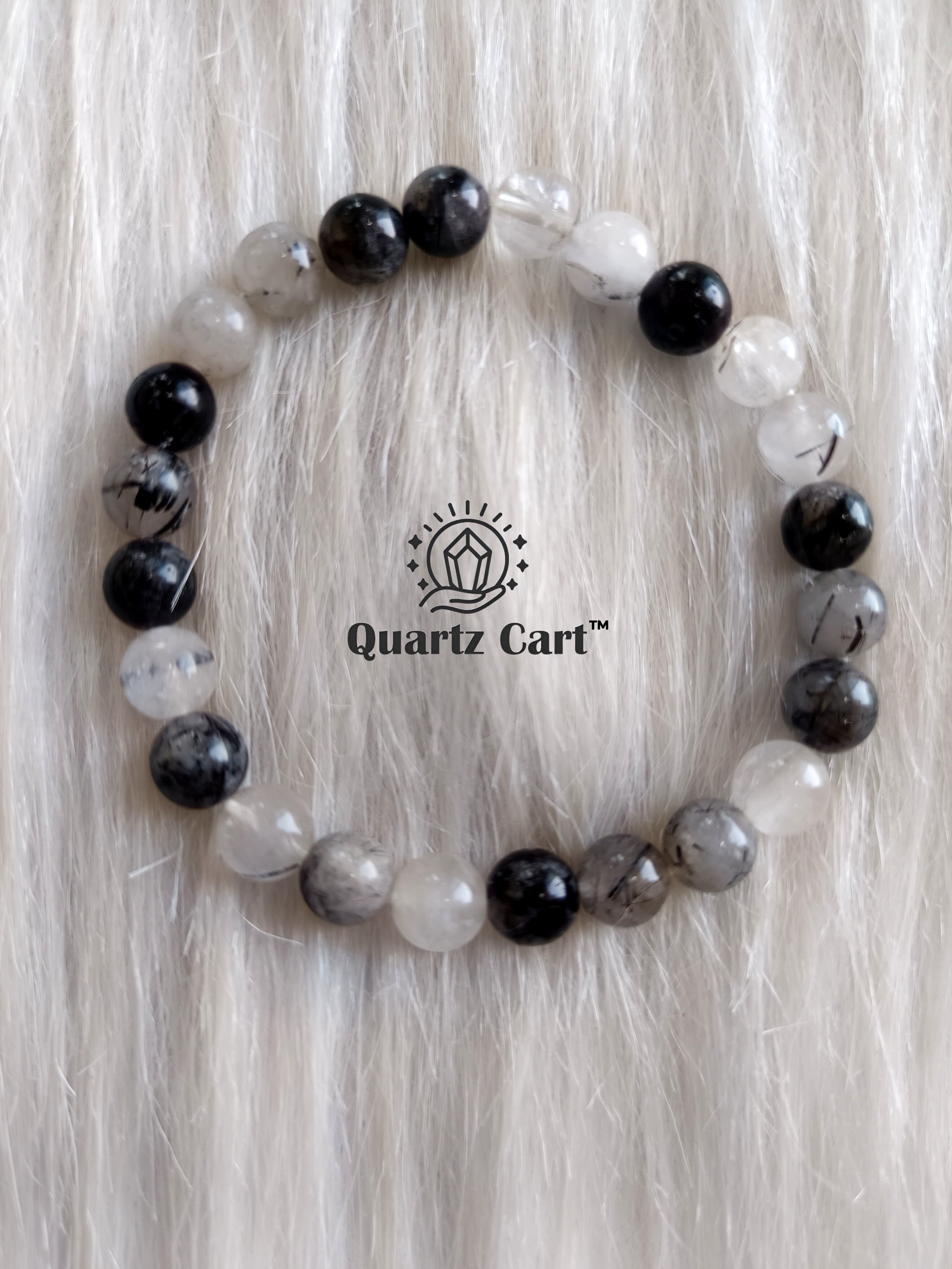 Tourmalinated quartz crystal bracelet with black tourmaline inclusions and clear beads placed on surface for protection and clarity