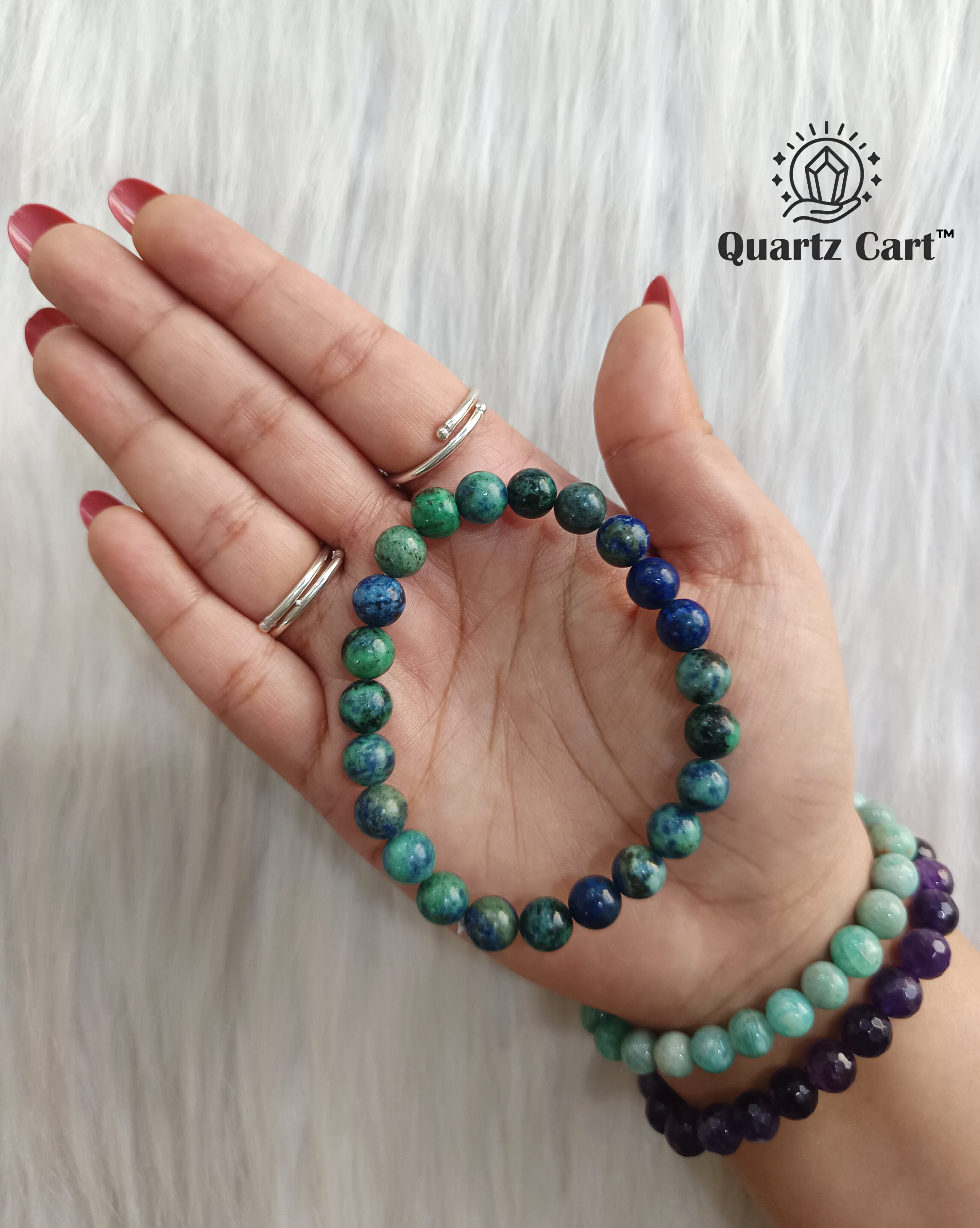 Hand wearing multiple beaded bracelets on a white background with 'Quartz Cart' branding.